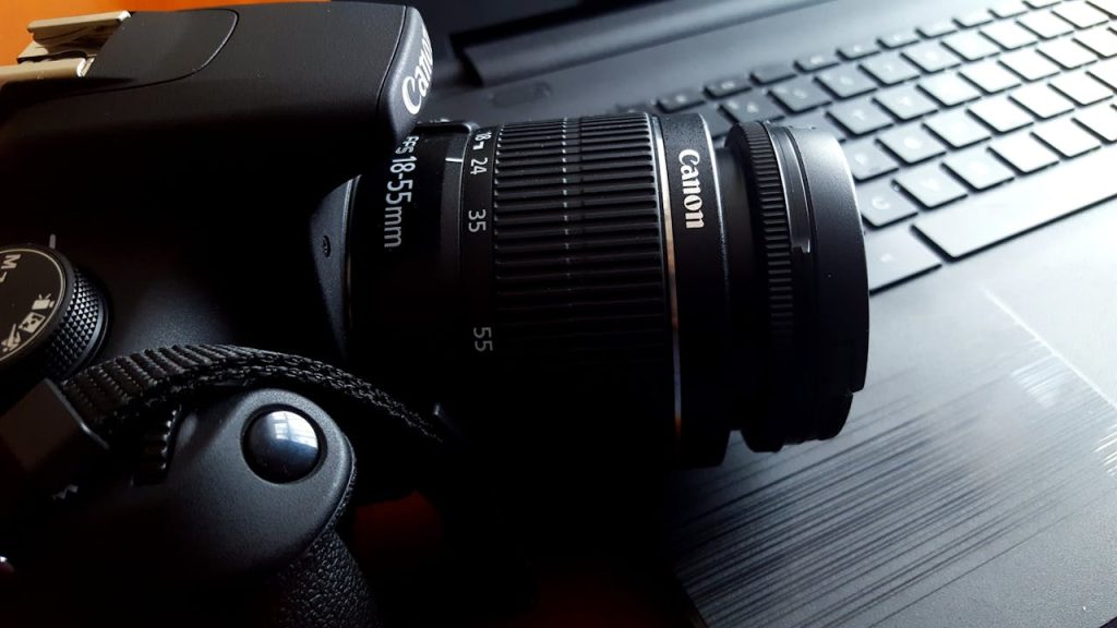 close-up-of-canon-camera-248519 Close-up of a black DSLR camera with lens on a laptop keyboard.